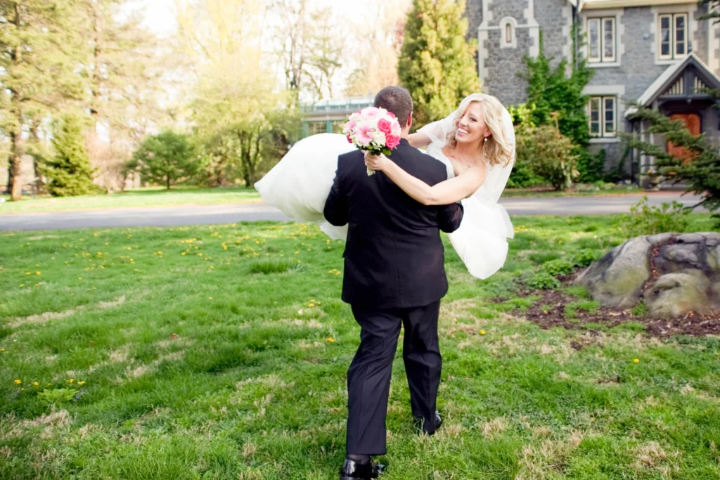 bride in grooms arms walking toward building