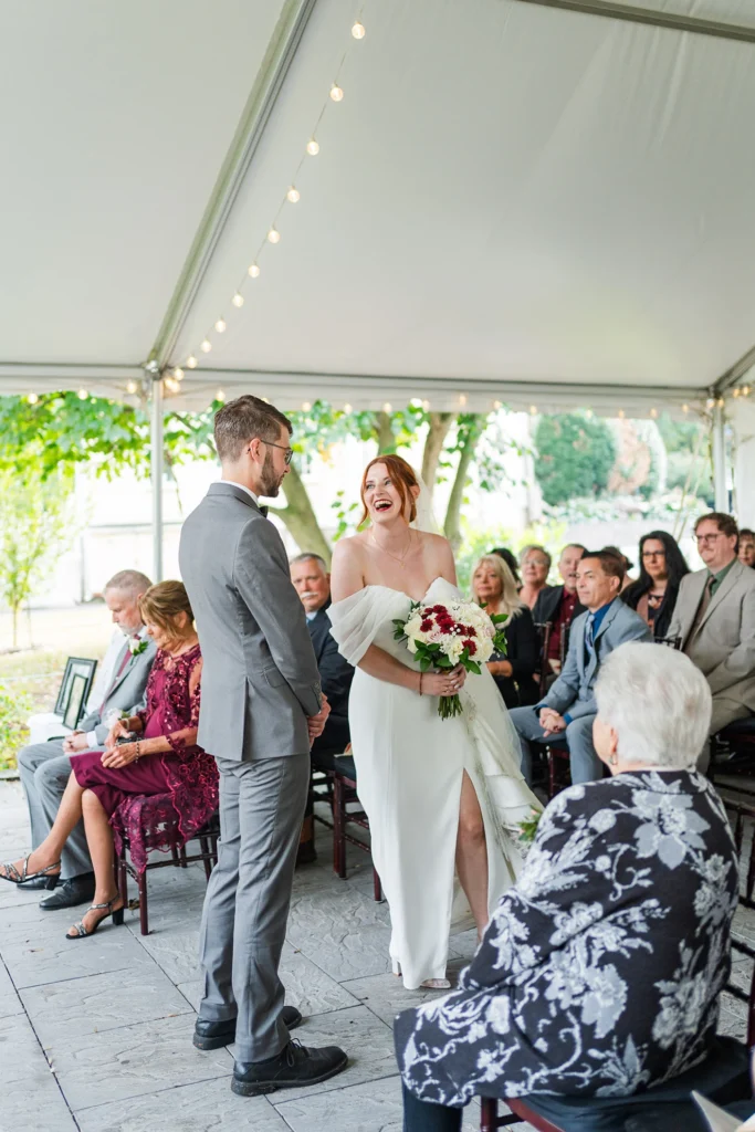 the bride and groom in the tent smiling an laughing with guests sitting during ceremony