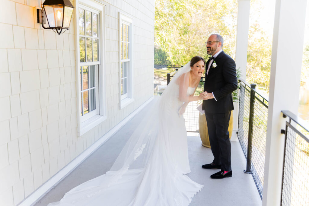 A relaxed, joyful moment as the bride leans forward laughing with her groom on a balcony at River House at Odette’s in New Hope, Pennsylvania.