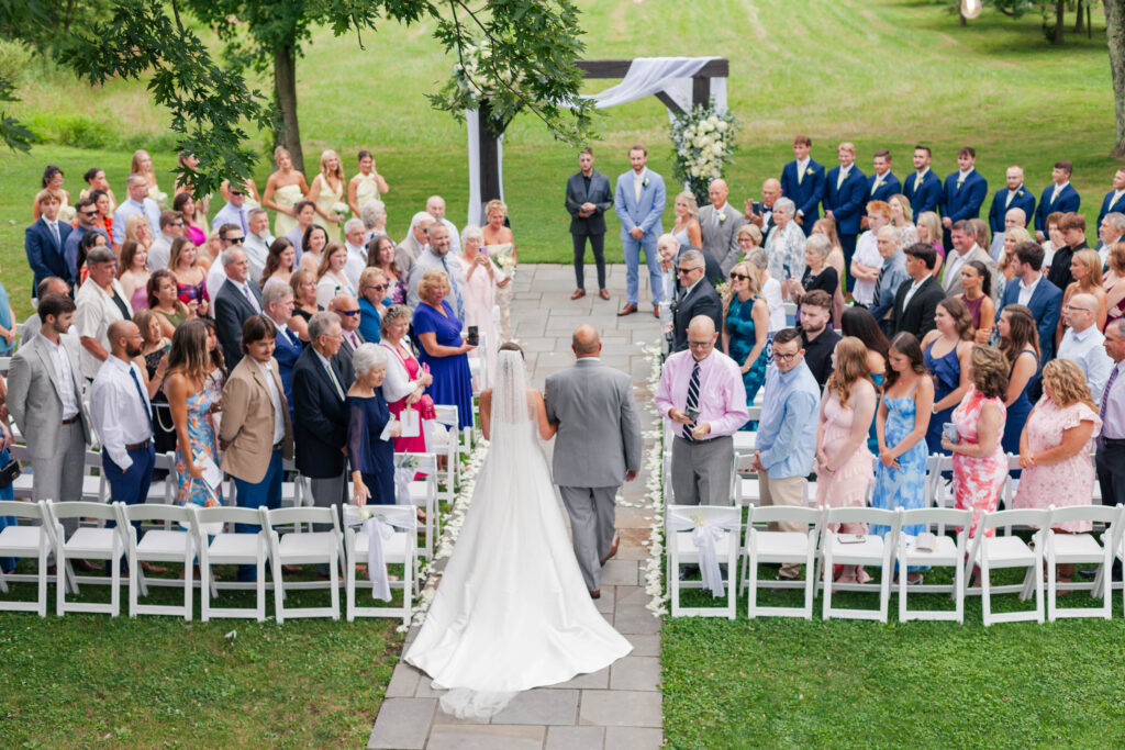 A bride walks down the aisle during an outdoor wedding ceremony at The Farm Bakery & Events in Quakertown, Pennsylvania.