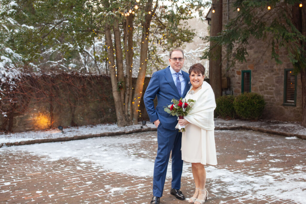 A joyful winter portrait outside Holly Hedge Estate in New Hope, Pennsylvania, where historic stone architecture and soft string lights create a warm atmosphere for Bucks County weddings.