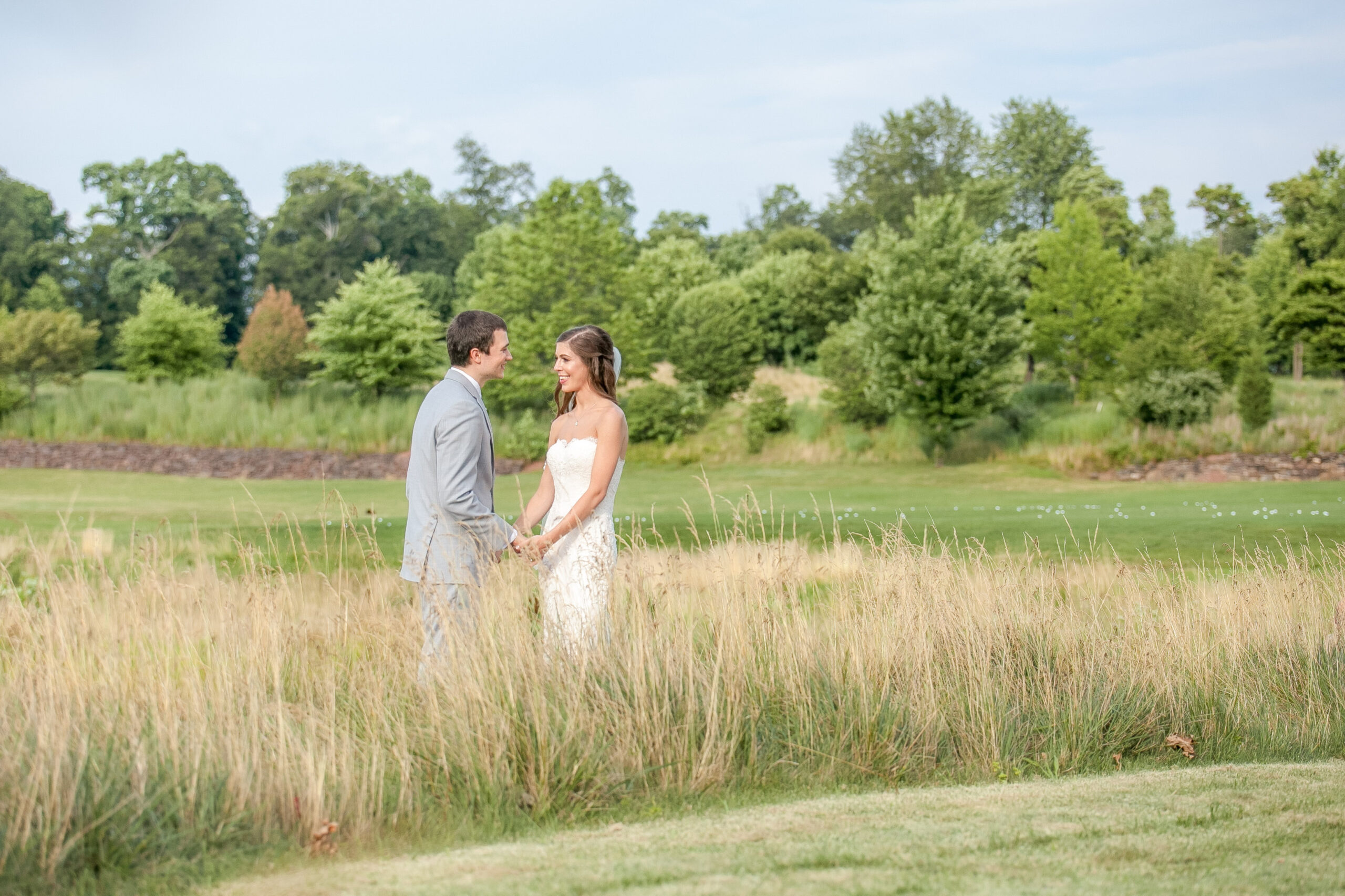 Bride and groom holding hands in tall grass during their RiverCrest wedding.
